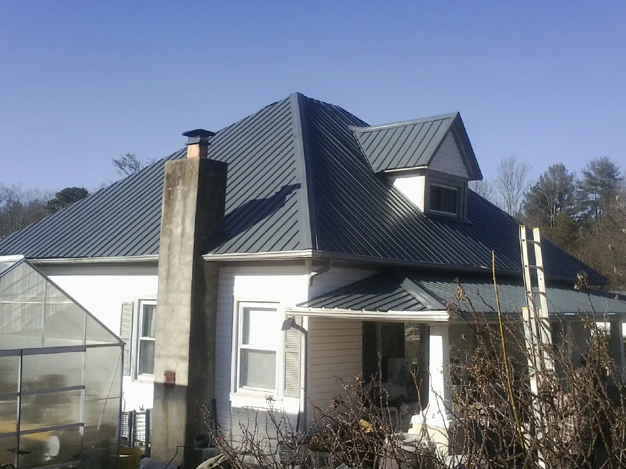 Dark blue standing seam metal roof on a white farmhouse with dormer — Slate & Tile Roof Repair by Roofing Brothers in Masonville