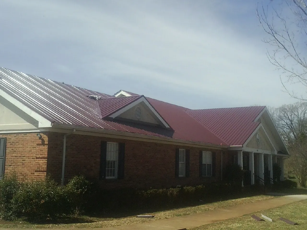 Red metal roof with gabled entries on a long brick building, from a Hail Damage Roof Repair job in Masonville