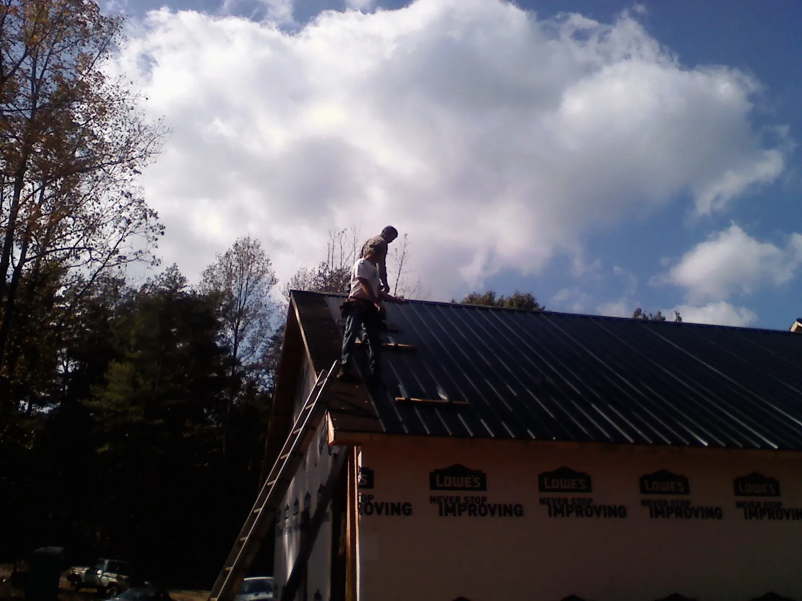 Roofer fastening dark metal panels high against a cloudy sky, from a Roof Inspection job in Masonville