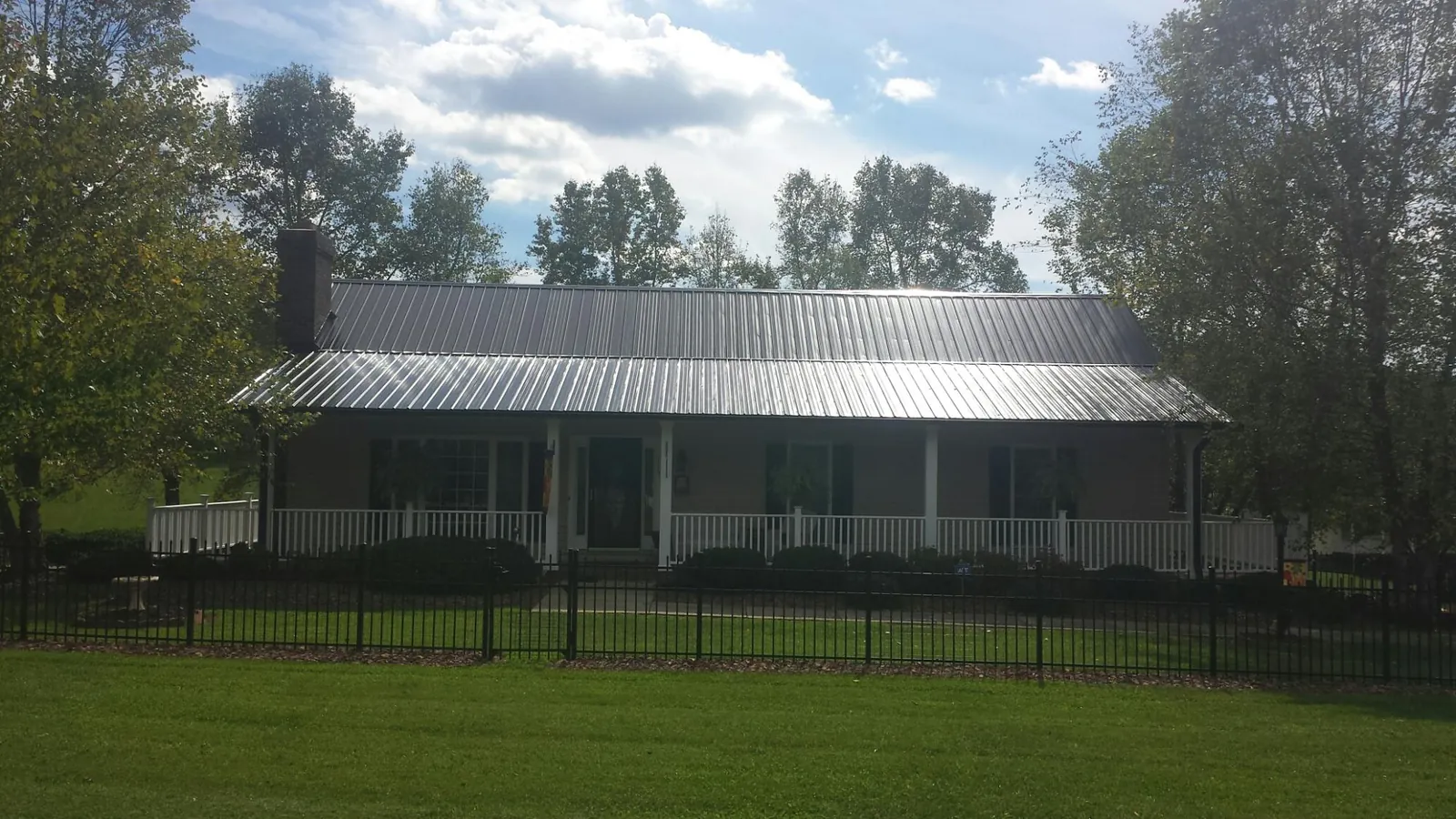 Gray metal roof on a brick ranch with a full width front porch — Gutter Guard Installation work by our crew in Masonville