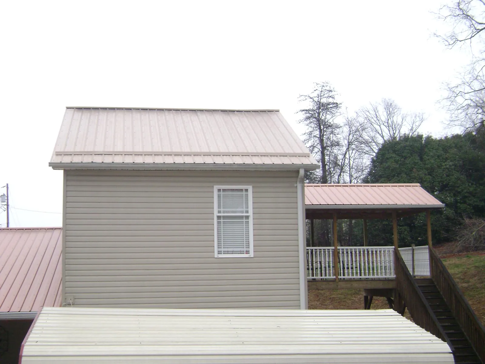 Tan metal roofs on a two story addition and attached porch, from a Roof Replacement job in Masonville